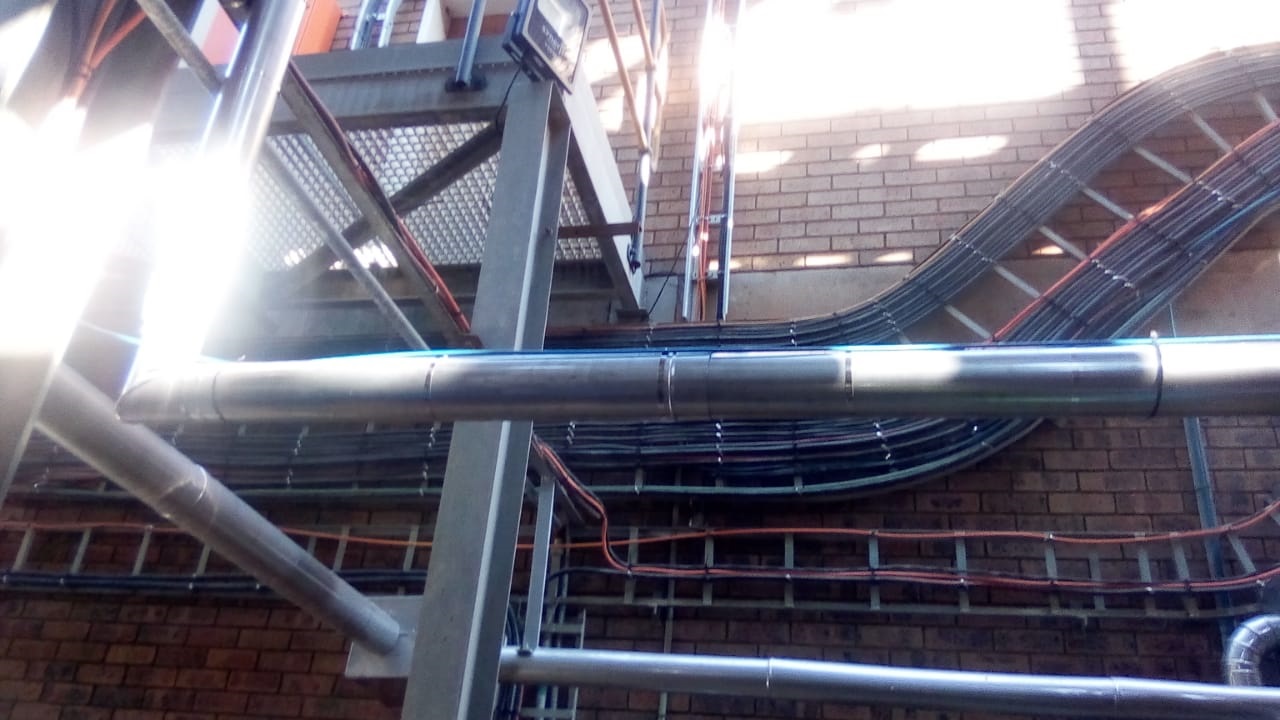Insulated pipework runs alongside cable trays in service corridor