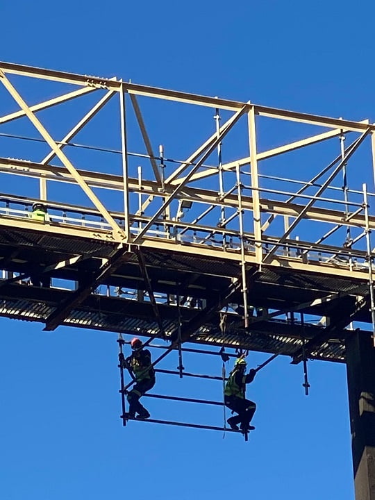 Riggers installing access platform beneath elevated steel gantry