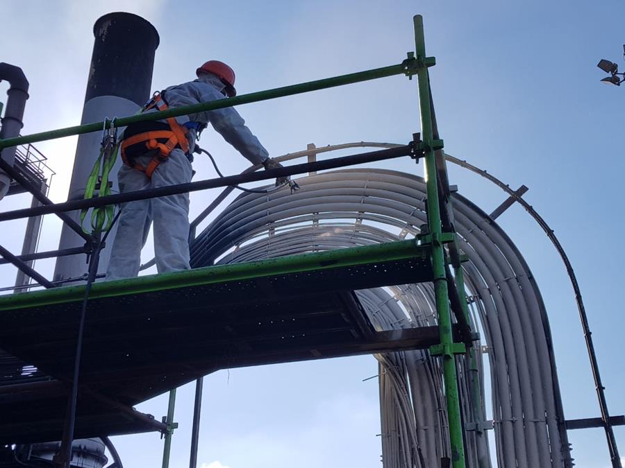 Applicator coating insulated pipework from scaffold platform at height