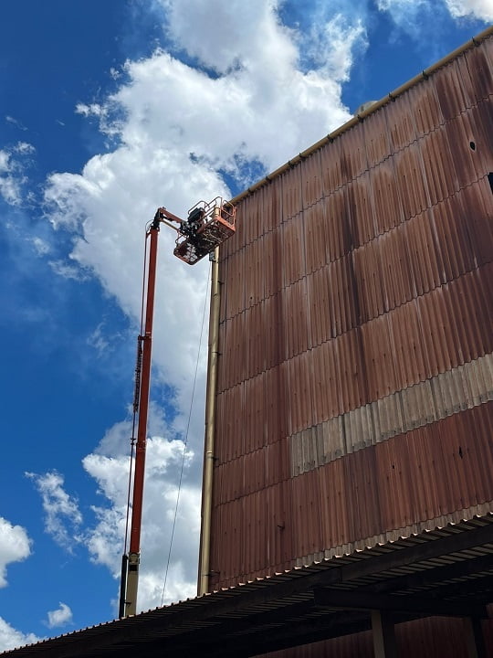 Telescopic boom lift accessing roof edge of large industrial building