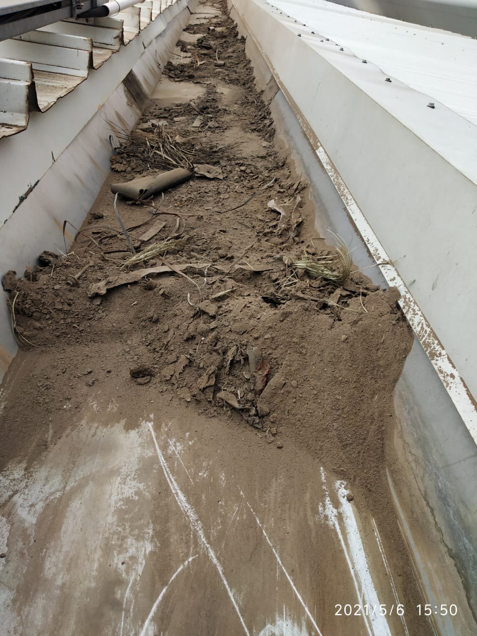 Industrial gutter heavily silted with mud and vegetation before cleaning