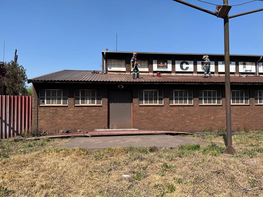 Crew refurbishing roof sheeting on industrial workshop building