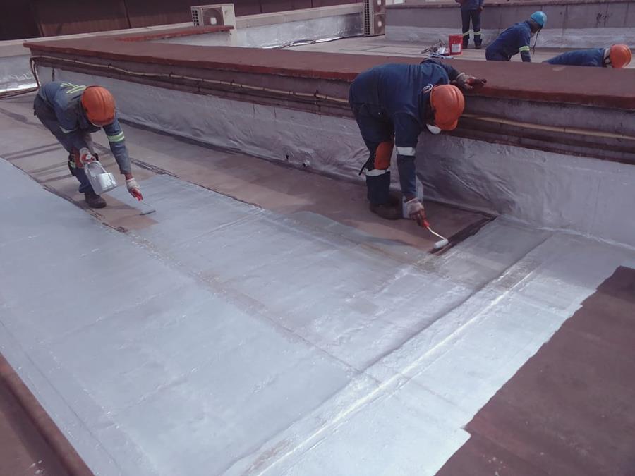Team applying waterproof coating system to large industrial roof