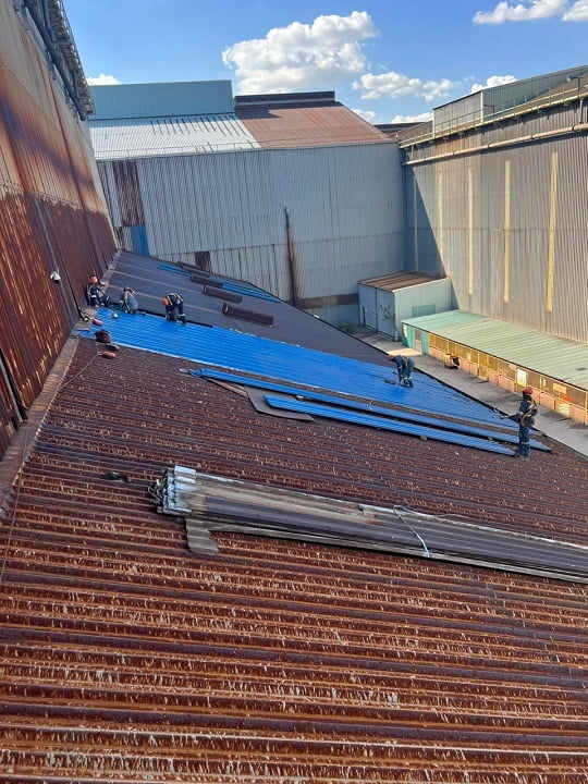 Crew installing new blue roof sheeting over rusted existing roof