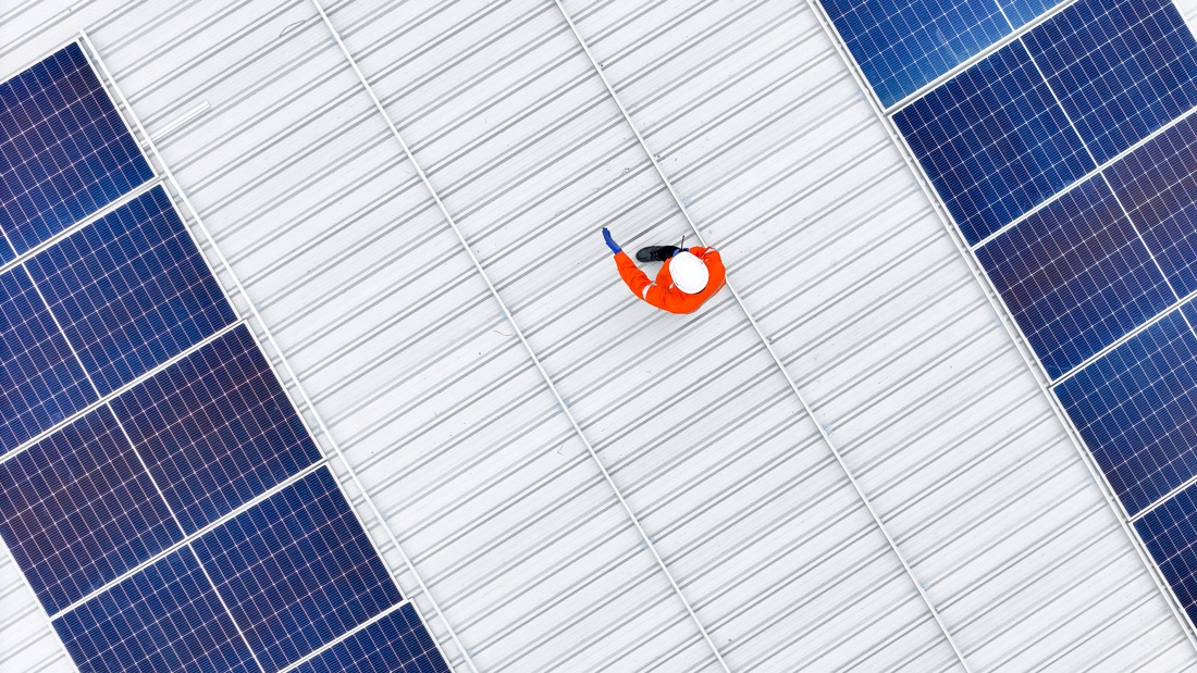 Aerial view of technician inspecting rooftop solar panel installation